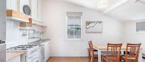 Una cocina con armarios blancos, una estufa y una zona de comedor con sillas de madera y una mesa.