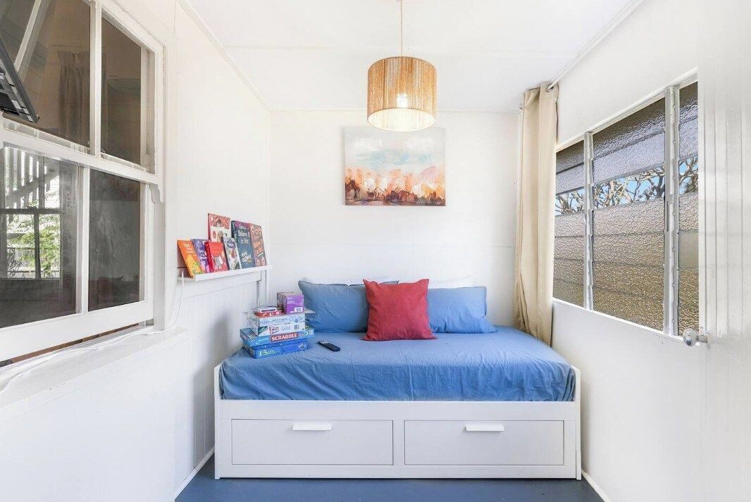 A bedroom with a bed, a window, a shelf with books, and a painting on the wall.