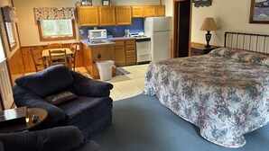 A compact room with a bed, a sofa, a small table, a kitchen area with wooden cabinets, a microwave, and a refrigerator. - Serene 1-bedroom cottage with Full Kitchen, TV, WIFI and AC in The Forks (The Forks)