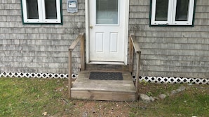 A house with a front door, two windows with shutters, a wooden porch, and a welcome sign. - Serene 1-bedroom cottage with Full Kitchen, TV, WIFI and AC in The Forks (The Forks)