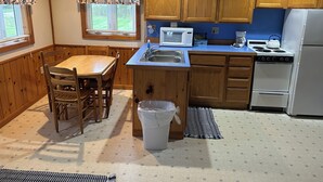 A compact kitchen with wooden cabinets, a dining table with chairs, a microwave, a stove, and a trash bin. - Serene 1-bedroom cottage with Full Kitchen, TV, WIFI and AC in The Forks (The Forks)