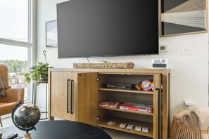 Huoneessa on suuri litteänäyttöinen televisio, puinen hylly, jossa on lautapelejä, maapallo ja ikkuna, josta on näkymä rakennuksiin.