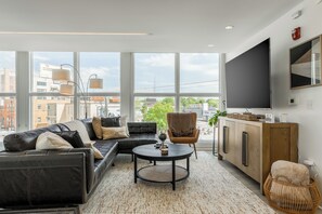 A modern living room with a sectional sofa, a round coffee table, a wooden cabinet, and a large TV. - Luxury High Rise Walkable Free Parking + Views (Kansas City)