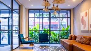 Eine moderne Lobby mit großen Fenstern, einem blauen Stuhl, einem braunen Sofa und einem Boden mit geometrischen Mustern.