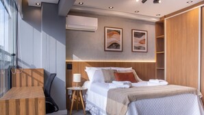 Ein modernes Hotelzimmer mit Bett, Nachttisch, Lampe, Klimaanlage, Kunstwerken und Holzvertäfelung.