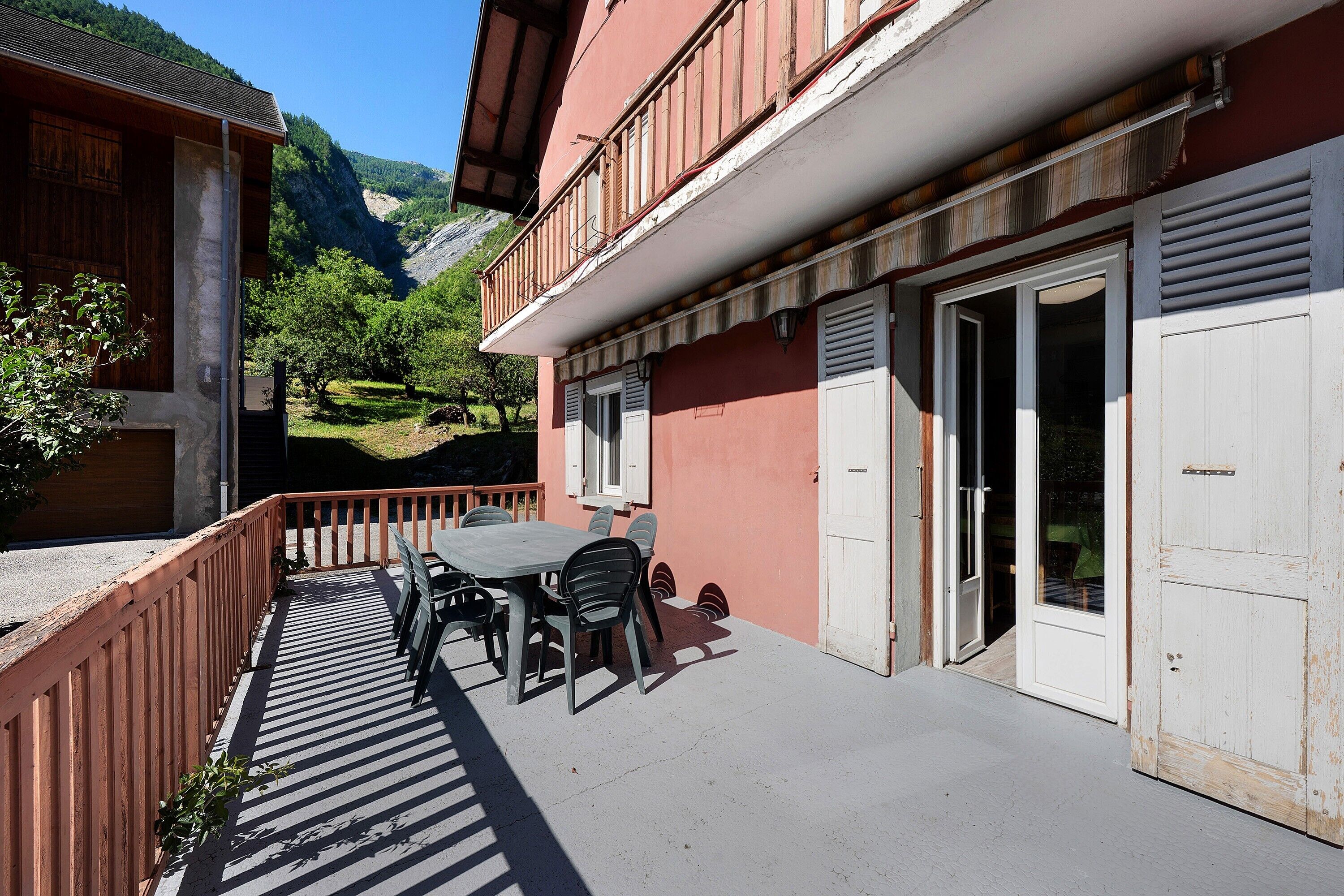 A balcony with a table and chairs, a wooden fence, and a mountain view.