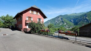 A red building with a balcony, surrounded by mountains and parked cars.