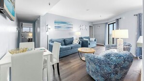 Una sala moderna con un sofá azul, una mesa de comedor blanca y un sillón estampado.