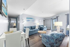 Ein modernes Wohnzimmer mit einem blauen Sofa, einem weißen Esstisch und einem gemusterten Sessel.