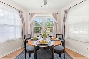 A dining area with a round table, four chairs, a vase with flowers, and a window with curtains. - Robin's Nest - Private Pool Retreat (North Myrtle Beach)