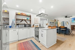 A modern kitchen with white cabinetry, a central island, and a dining area with a bar. - Robin's Nest - Private Pool Retreat (North Myrtle Beach)