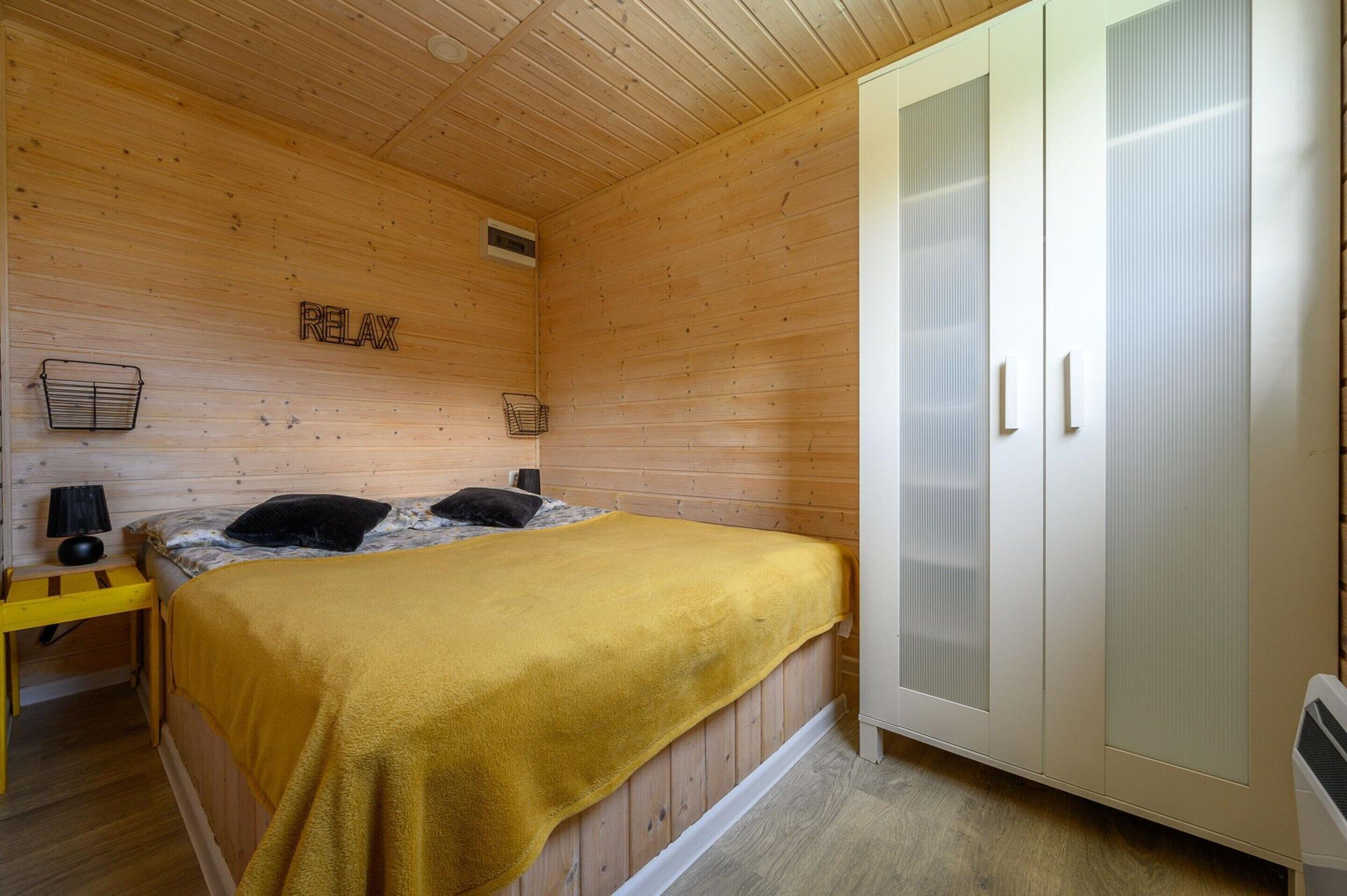 Ein Zimmer mit Holzboden, einem Bett, einem Schrank und einem kleinen Tisch mit Lampe.