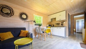 Un interior moderno con techo de madera, una zona de comedor con sillas amarillas, una cocina con armarios blancos y un sofá con cojín amarillo.