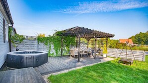 Un patio trasero con jacuzzi, terraza de madera, pérgola y mobiliario exterior.