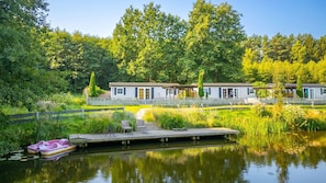 Una cabaña junto al lago con un muelle, rodeada de vegetación exuberante y árboles.