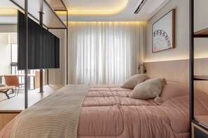 Ein modernes Hotelzimmer mit Bett, Schreibtisch, Sessel und Fernseher.