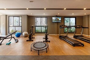 Ein Heimfitnessraum mit Trainingsgeräten, großen Fenstern und einem Fernseher.