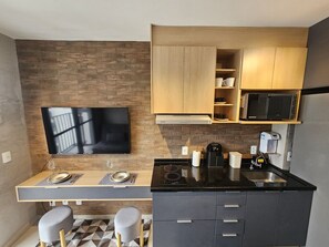 A compact kitchen with a flat-screen TV, a microwave, and a coffee machine. - Studio Clean - Pinheiros (São Paulo)