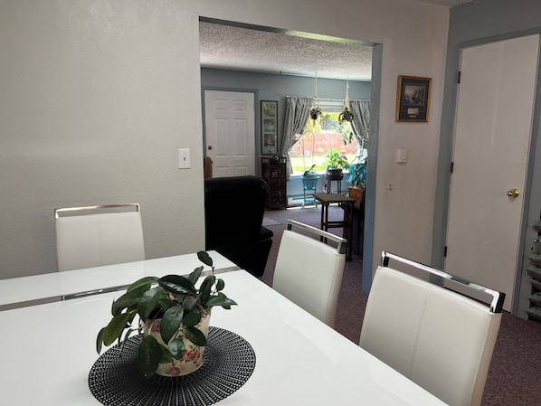 Ein Essbereich mit Tisch, Stühlen, einem Blumentopf und Blick in einen Raum mit Tür und Fenster.