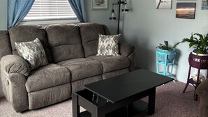 Ein Wohnzimmer mit Sofa, Couchtisch, Wandlampe und einem Fenster mit Vorhängen.