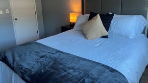 Ein ordentlich gemachtes Bett mit Kopfteil, einer Nachttischlampe und einer Tür links.