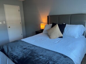 Ein ordentlich gemachtes Bett mit Kopfteil, einer Nachttischlampe und einer Tür links.