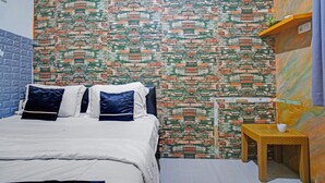 Une chambre avec un mur décoré d’un motif en briques, un lit avec une literie blanche et des coussins bleus, une petite table en bois et un mur bleu sur un des côtés.