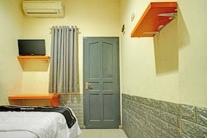 Een kamer met een bed, een televisie op een standaard, een deur en een radiator.