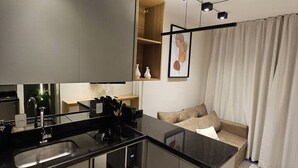 Une cuisine moderne dotée d’un plan de travail noir, d’un évier intégré et d’un four encastré. On trouve une étagère en bois au-dessus de l’évier et une œuvre d’art encadrée au mur.