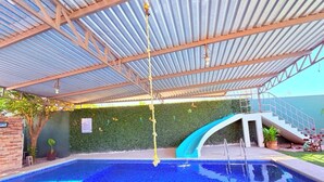 An indoor swimming pool with a metal roof, a staircase, and a green wall with a small plant. - Casa Completa: Confort, Alberca y Asador. (Fraccionamiento El Chaparral)
