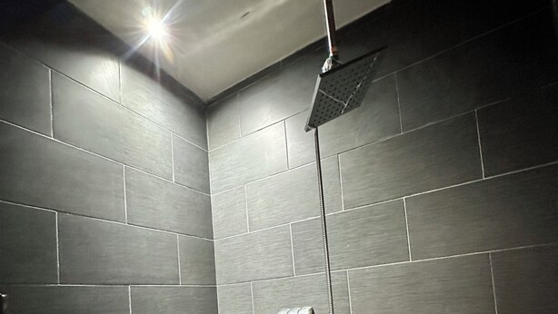 A modern shower area with dark tiles, a bench, and a handheld showerhead. - Casa Completa: Confort, Alberca y Asador. (Fraccionamiento El Chaparral)