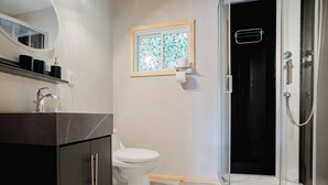 Moderni kylpyhuone, jossa on wc, suihku, peilillä varustettu pesuallas ja ikkuna, jonka lasissa on lehtikuvio.