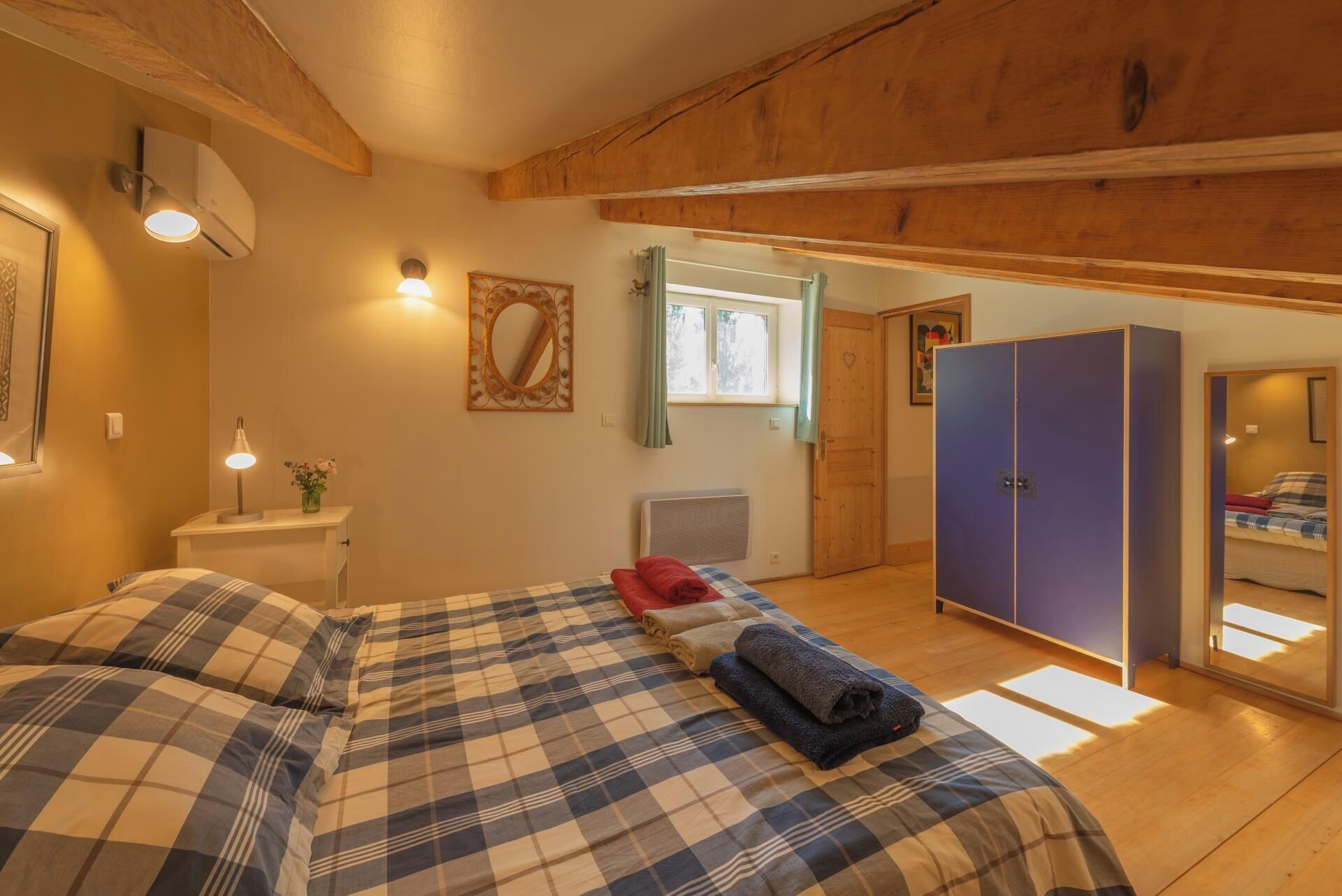 Ein Schlafzimmer mit einem Bett, einer Nachttischlampe, einem Spiegel, einem Fenster mit Vorhängen, einem Heizkörper und einem Kleiderschrank.