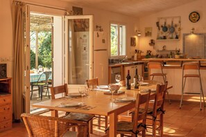 Un coin repas avec une table dressée pour six personnes, une cuisine en arrière-plan et une porte-fenêtre coulissante donnant sur un espace extérieur.