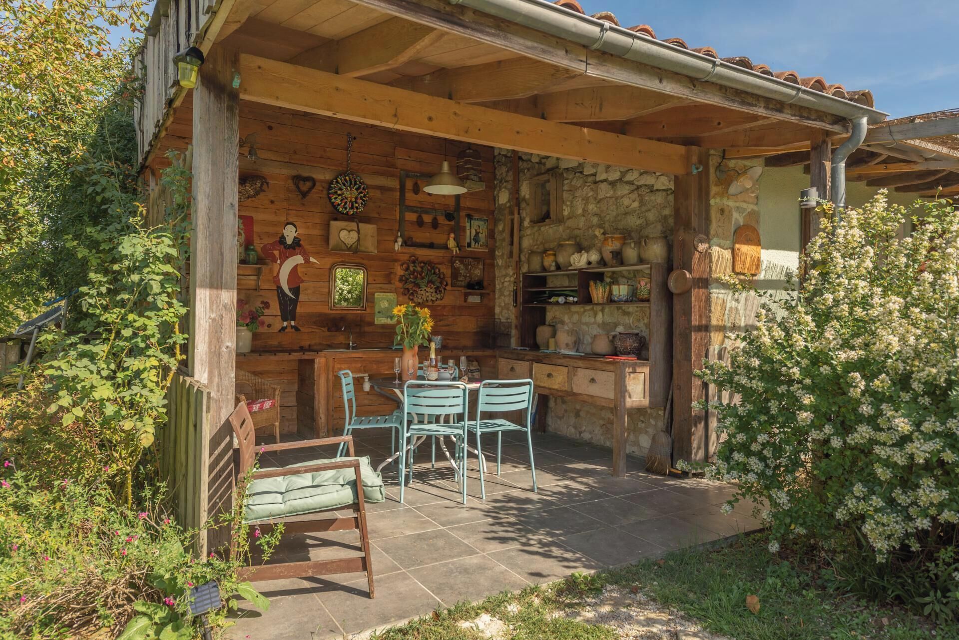 Une cuisine rustique en bois, avec un mur en pierre, un coin repas comprenant une table et des chaises, et un petit jardin.