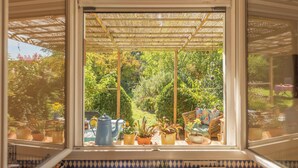 Ein Wintergarten mit Blick auf einen üppigen Garten, ein Tisch mit Topfpflanzen und ein blauer Wasserkocher.