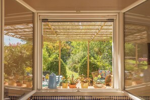 Une v éranda donnant sur un jardin luxuriant, une table ornée de plantes en pot et une bouilloire bleue.