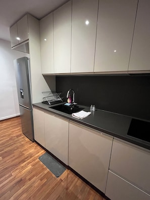 Eine moderne Küche mit grauen Schränken, einer schwarzen Arbeitsplatte und einem Edelstahl-Kühlschrank.