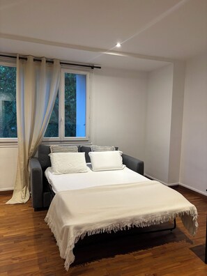 Ein Schlafzimmer mit einem Bett, einem fensterbelaubten Fenster, einer Couch und Holzboden.