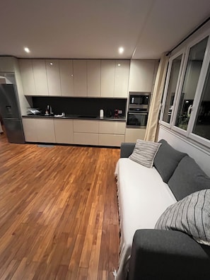 Eine moderne Küche mit eingebauten Geräten, Holzboden und einem grauen Sofa mit gestreiftem Kissen.
