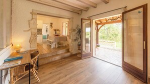 Et rustikt interiør med et træspisebord, fletstole, en trappe til en patio og udsigt til grøn vegetation udendørs.