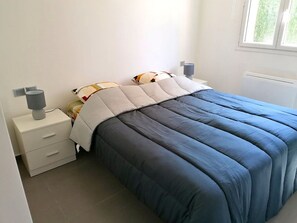 Ein Schlafzimmer mit einem Bett, Nachttischen, einer Lampe und einem Fenster.