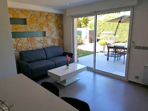 Ein modernes Wohnzimmer mit einer Steinwand, einem grauen Sofa, einem weißen Couchtisch und einer Glastür, die auf eine Terrasse im Freien führt.