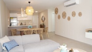 A modern living room with a sofa, a dining table with chairs, a kitchen area with a stove, and decorative wall art. - Modern 2 Bed 2 Bath apartment in Playa Nueva Romana - Beach, PGA Golf and Pools (La Caña)