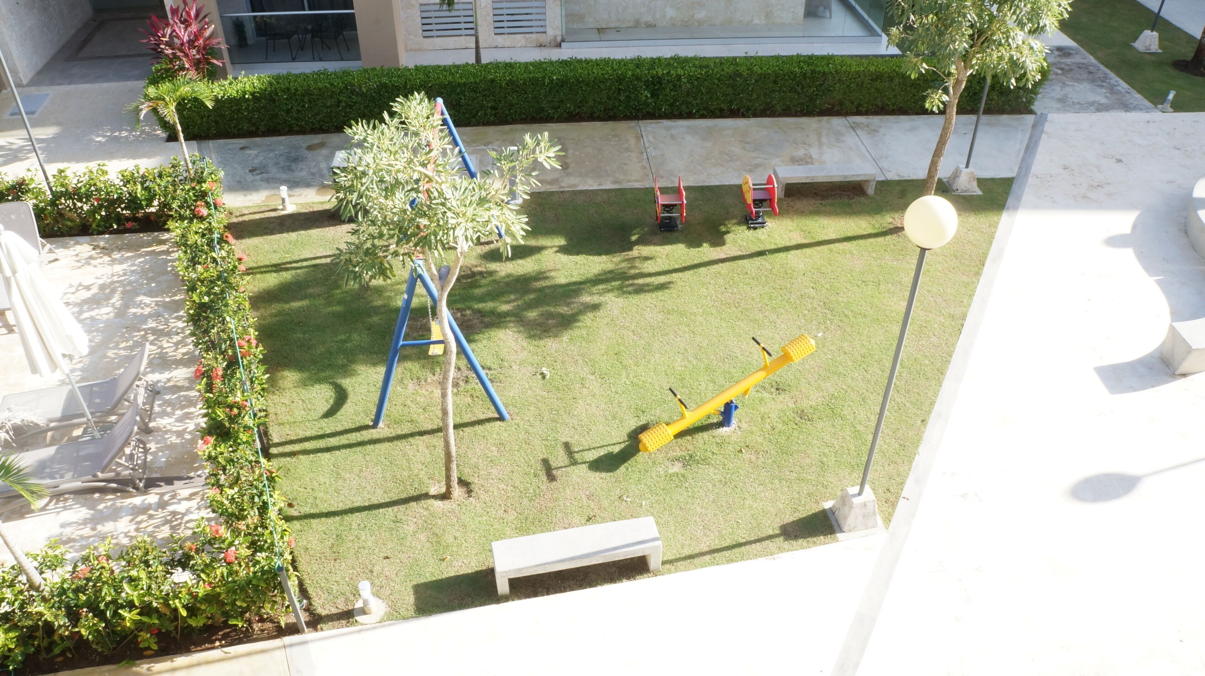 Une cour avec une aire de jeux, un banc et une haie.