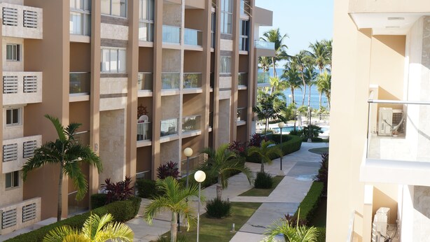A multi-story hotel with balconies, a pool area, and palm trees. - Modern 2 Bed 2 Bath apartment in Playa Nueva Romana - Beach, PGA Golf and Pools (La Caña)
