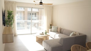En moderne stue med sofa, sofabord, en plante og en skydedør, der fører ud til en balkon.
