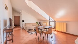 Et spiseområde med et bord og stole, en sofa og et fjernsyn på et skab.