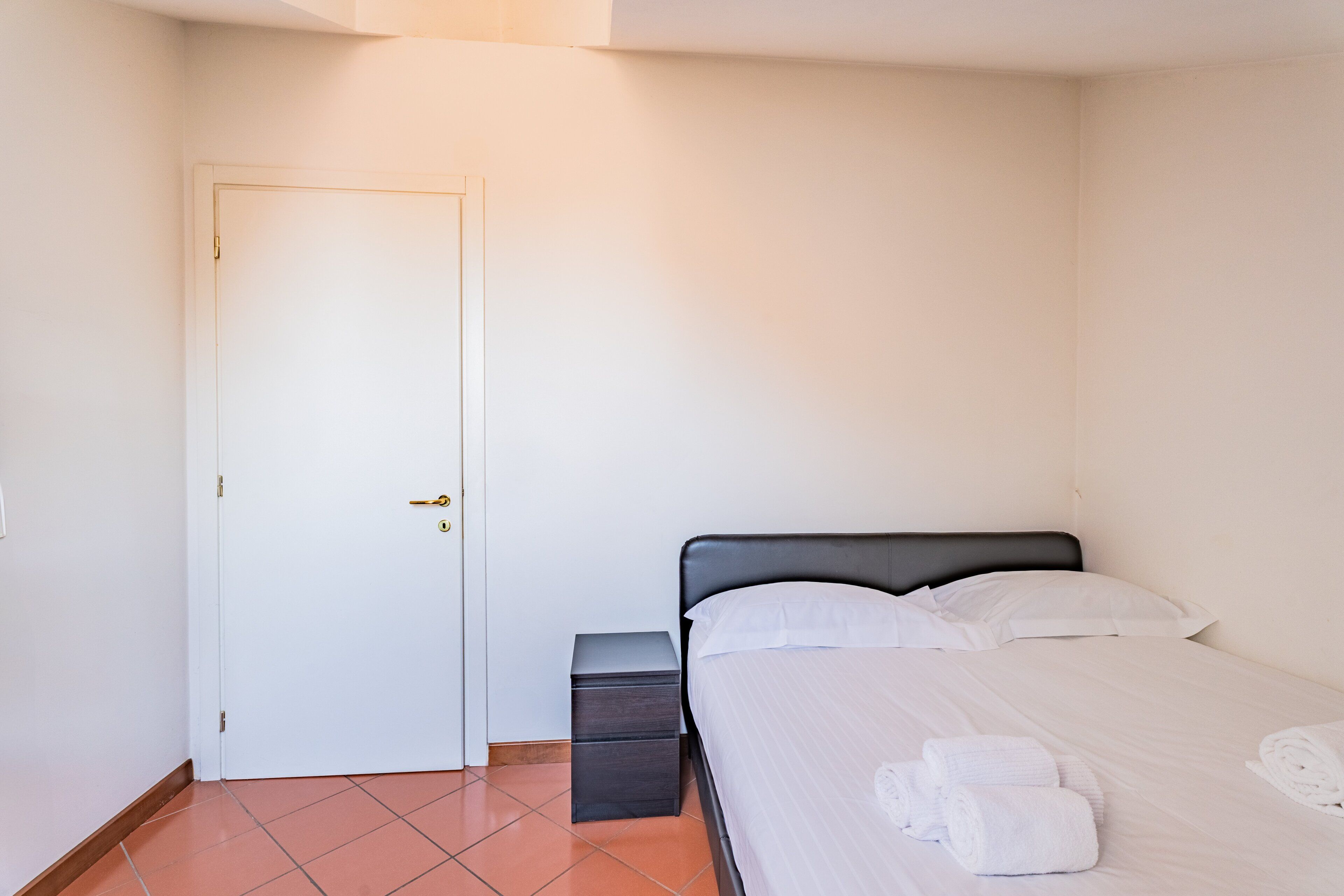 A room with a bed, a nightstand, a door, and a tiled floor.