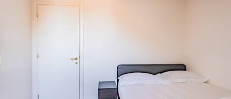 A room with a bed, a nightstand, a door, and a tiled floor.